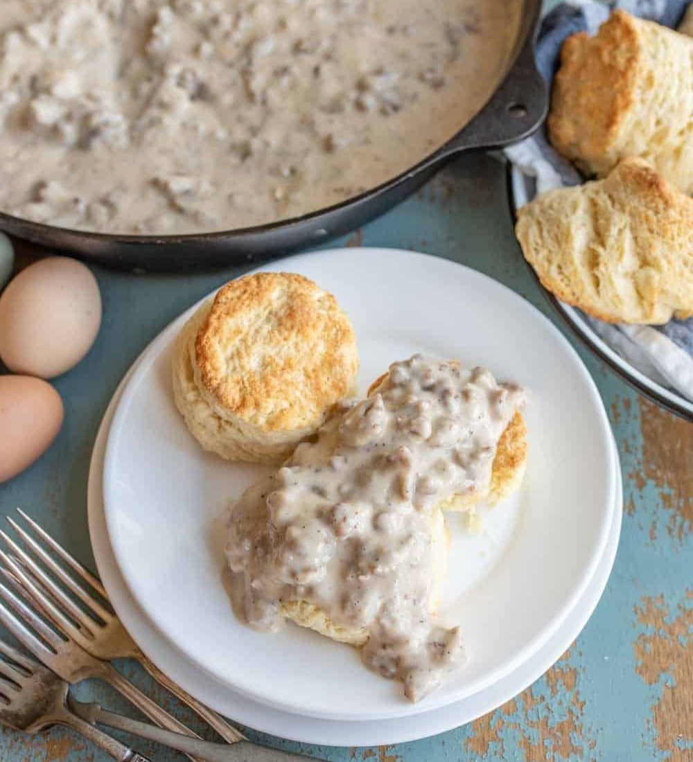 Pork sausage gravy served over biscuits on a plate with forks and farm fresh eggs