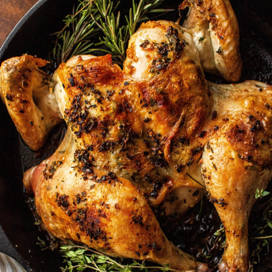 Deliciously roasted spatchcocked chicken with herbs in a cast iron pan on a bed of fresh green herbs,
