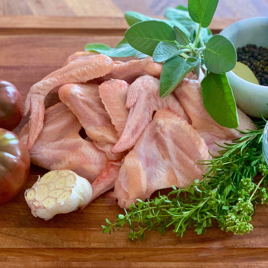 Organic pasture raised chicken wings with herbs, fresh garlic and tomato, and seasonings on wood cutting board.