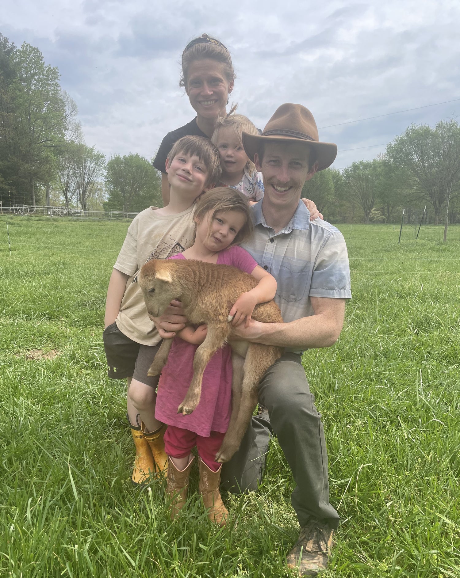 Melvin Hill Meats owner family on farm with lamb in pasture.