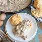 Pork sausage gravy served over biscuits on a plate with forks and farm fresh eggs