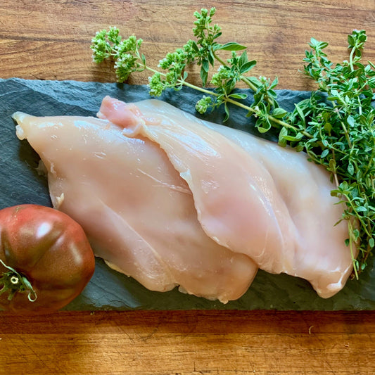 Organic pasture raised boneless skinless chicken breasts on slate with herbs and tomato